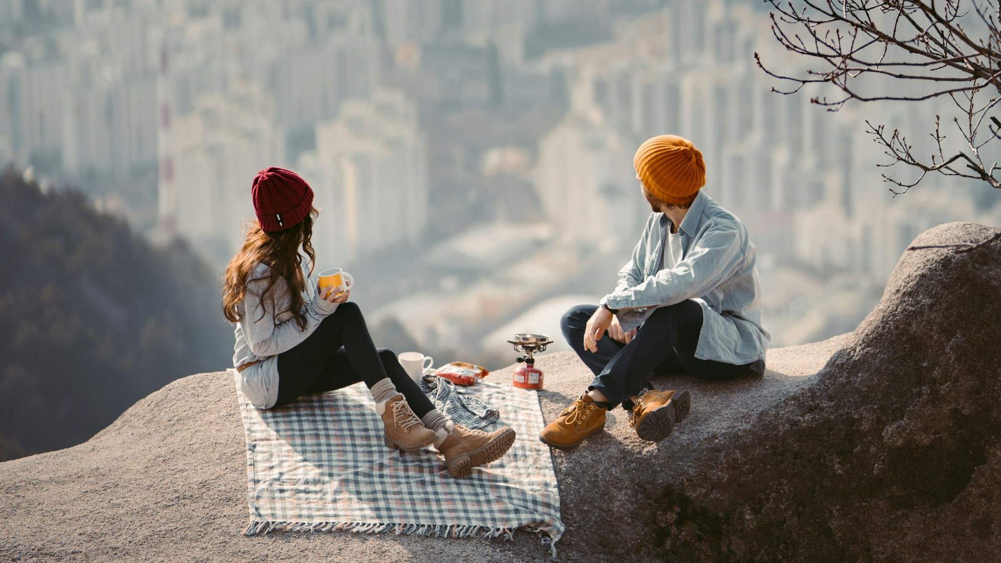 Couple enjoying a scenic picnic with a breathtaking view of the Seoul skyline from a mountain cliff.